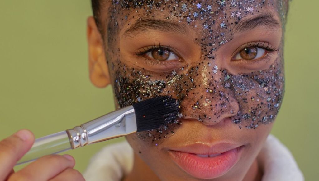 dark skin girl applies glitter face mask starlets