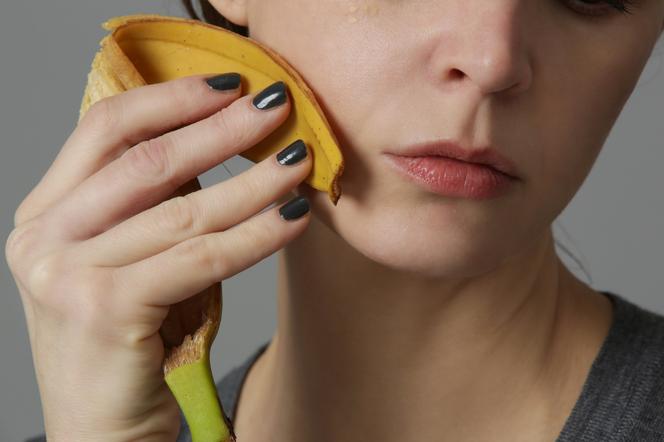A woman rubs her face with a banana peel