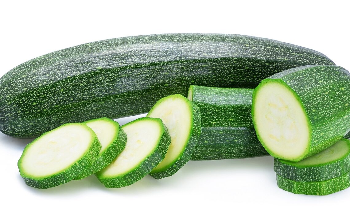 Zucchini und Zucchini-Scheiben vor weißem Hintergrund